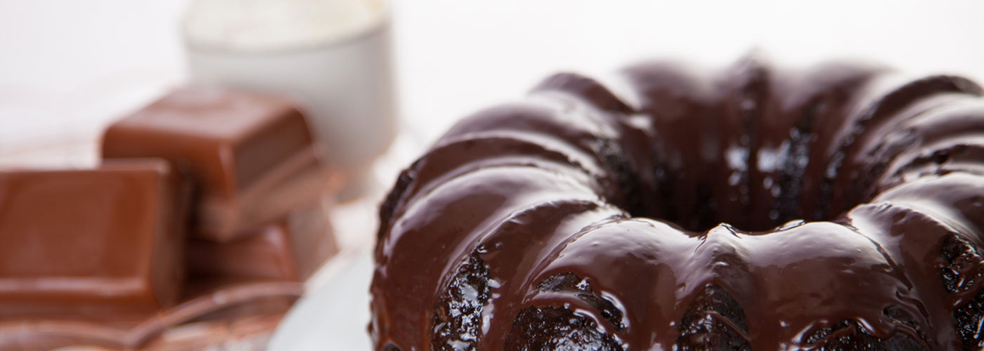 Lifestyle image of a Chocolate Cake with chocolate frosting on a white cake stand