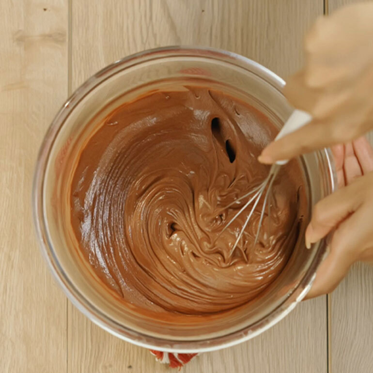 Chocolate cake in a clear bowl with a whisk