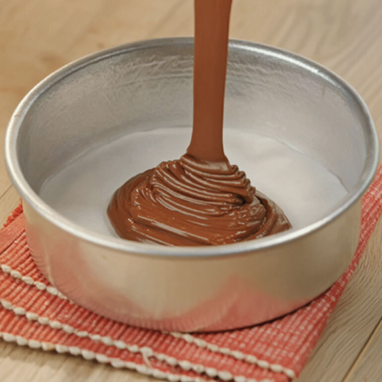 Chocolate cake mix being poured into a tall round baking pan