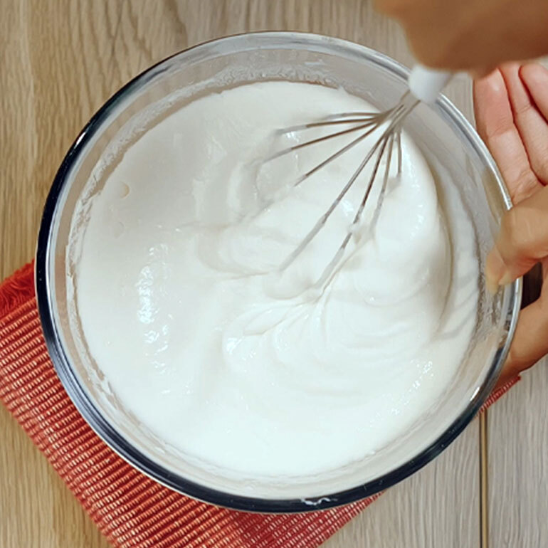 White mixture in a clear bowl and a whisk