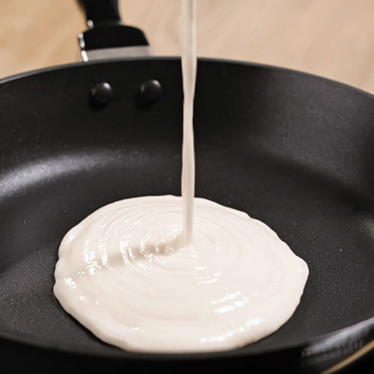 White batter being poured into a skillet