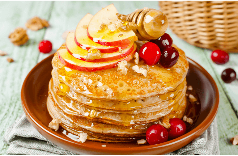 Apple crisp pancakes stacked on a plate with fruit and syrup on top