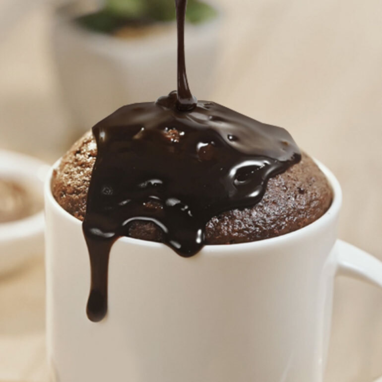 A close up image of a white mug treat with chocolate sauce poured on top