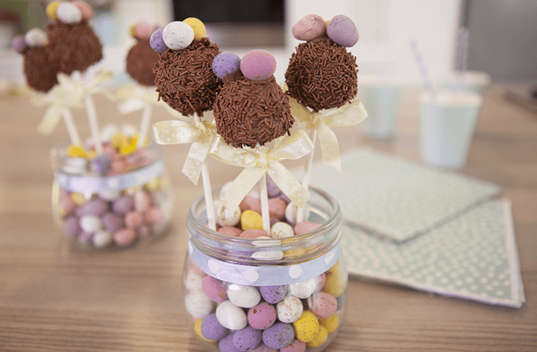 Chocolate sprinkled covered cake batter pops in a glass jar with multi-colored candy eggs in the bottom