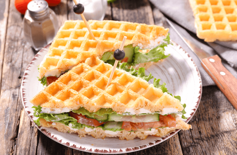 Two slices of Grilled Cheese Wafflewiches on a white plate with a pepper shaker in the background