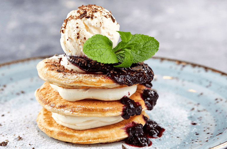 A plate of a Pancake Ice Cream Sandwiches with a scope of ice cream, mint and jam sauce