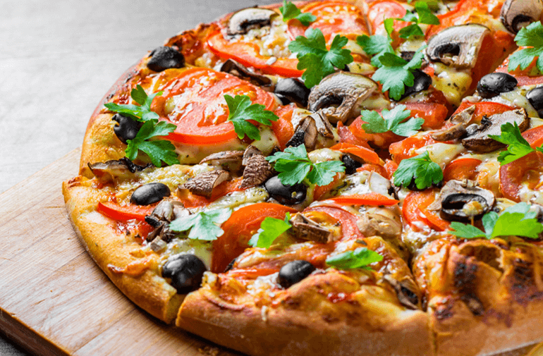 A Pancake Pizza with tomatoes, mushrooms and mint leafs on a wood cutting board