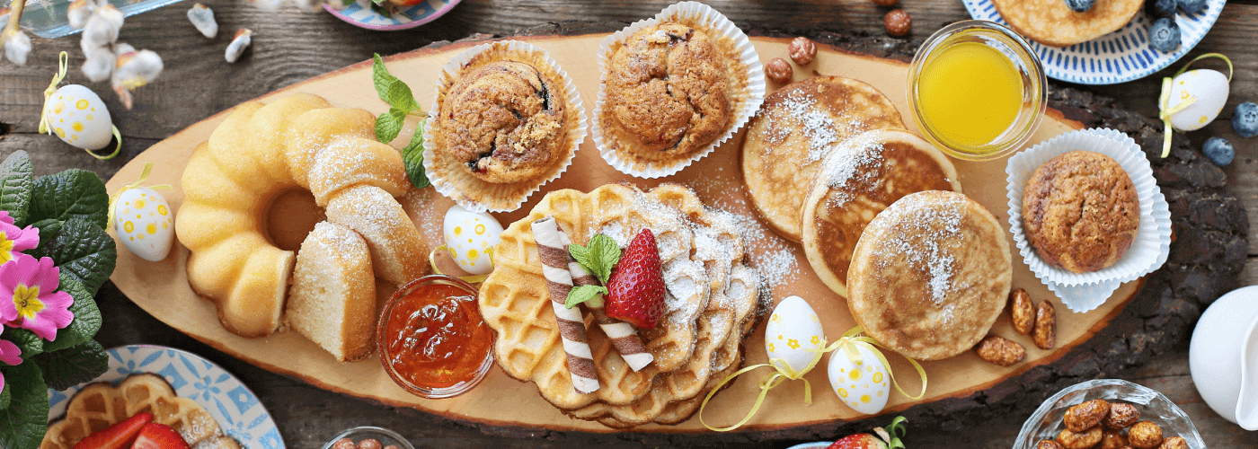 A table of various food such as pancakes, pastries, fruit, cake and nuts