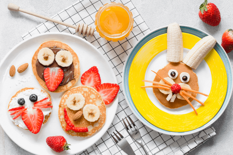 Pancakes decorated to look like animals using bananas, strawberries, carrots and blueberries